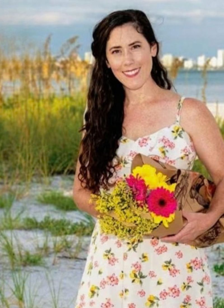 Miranda,founder of Siesta Social Events, holding a colorful bouquet of flowers outdoors along the Southwest Florida coast.