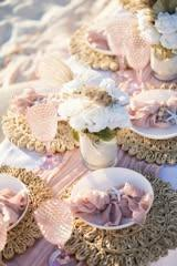 Elegant outdoor event table with pink dinnerware, folded napkins, and soft floral centerpieces.