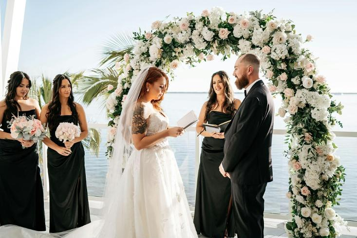 Bride and groom exchanging vows beneath a floral wedding arch with an Officiant during a Sarasota wedding ceremony.