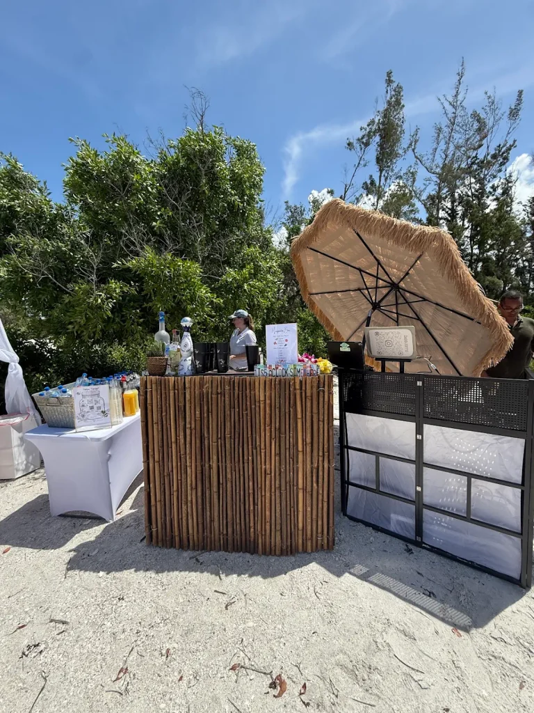 Beachfront event featuring a bamboo mobile bar, tropical umbrella, and DJ setup coordinated by Siesta Social Events