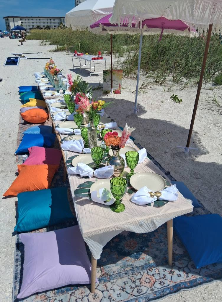 Long beach dining table with colorful pillows and coordinating tableware for a Sarasota corporate event.