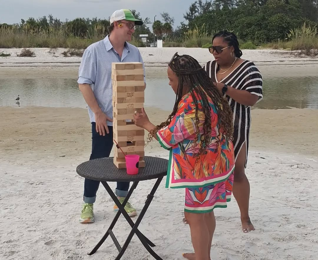 Guests playing giant Jenga on the beach during a casual outdoor celebration.