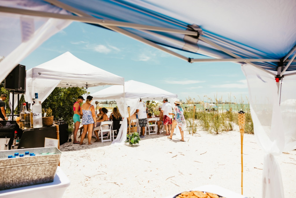 Guests gathering beneath a large white canopy at sn outdoor beach event in Sarasota Florida.