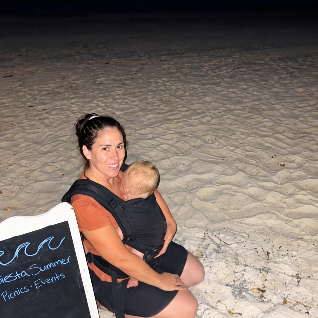 Miranda holding her baby in a front carrier during the early days of her beach event planning bussiness