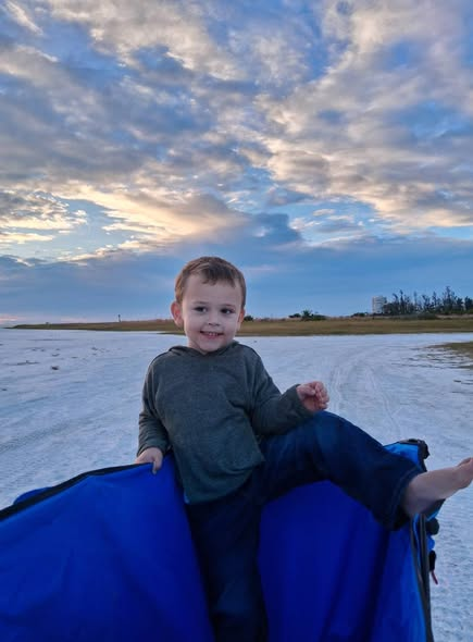 Miranda's young son sitting on the beach equipment besides the water during a family outing