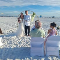 Bride and groom standing beneath a circular floral wedding arch on a Florida beach with seated guests.