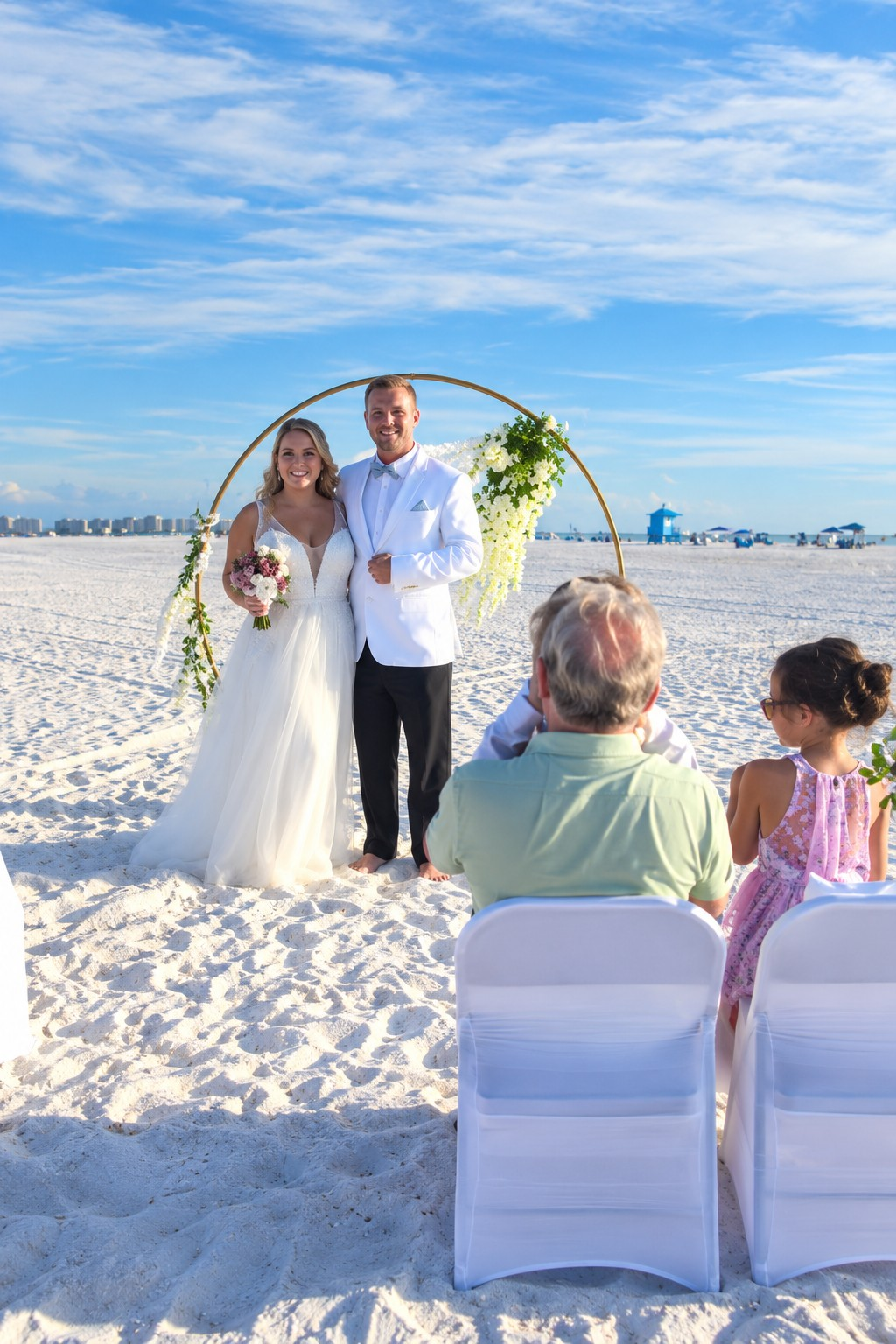 Wedding ceremony planning in Sarasota featuring a bride and groom beneath a circular floral arch on the beach.