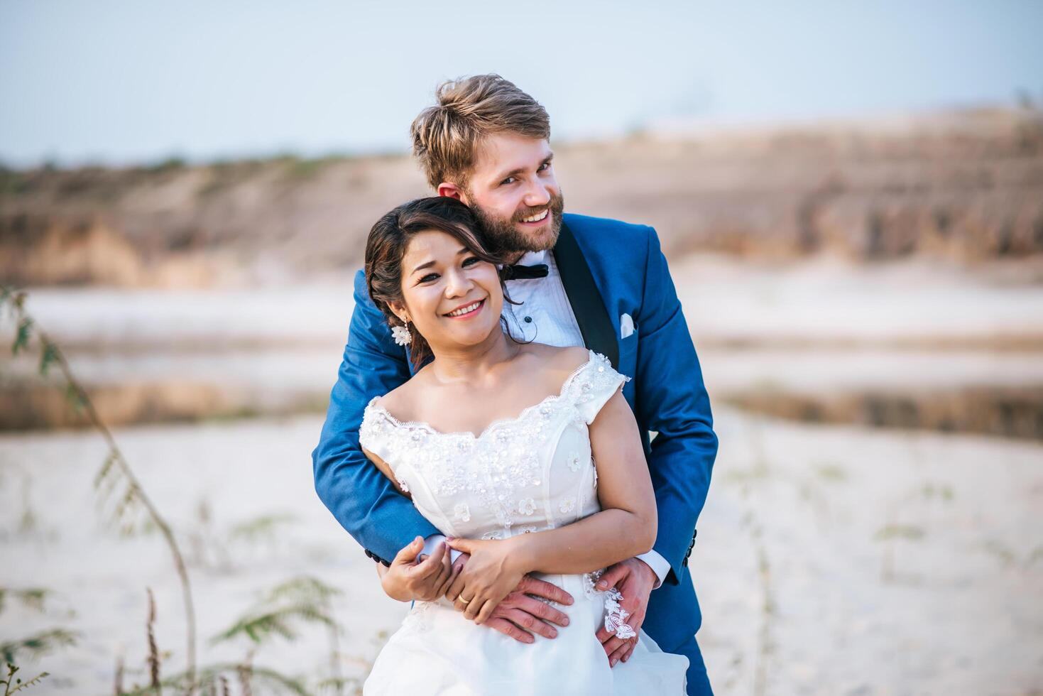 Newlywed couple embracing outdoors,with the bride holding a bouquet and the groom wearing a blue suit.